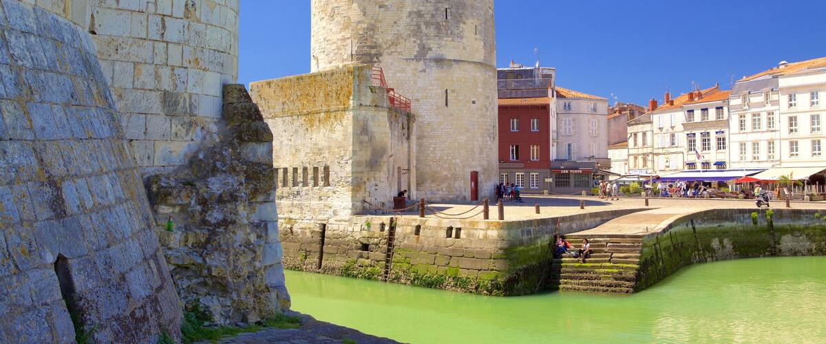 A historic stone tower with a flag, a moat, and a town with buildings and people.