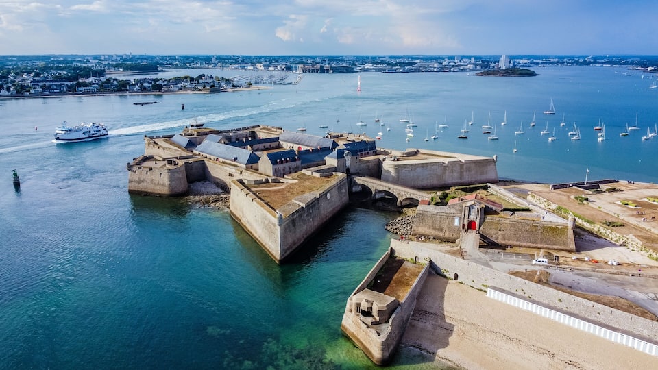 A coastal fortification with a harbor, surrounded by a cityscape and a clear sky.