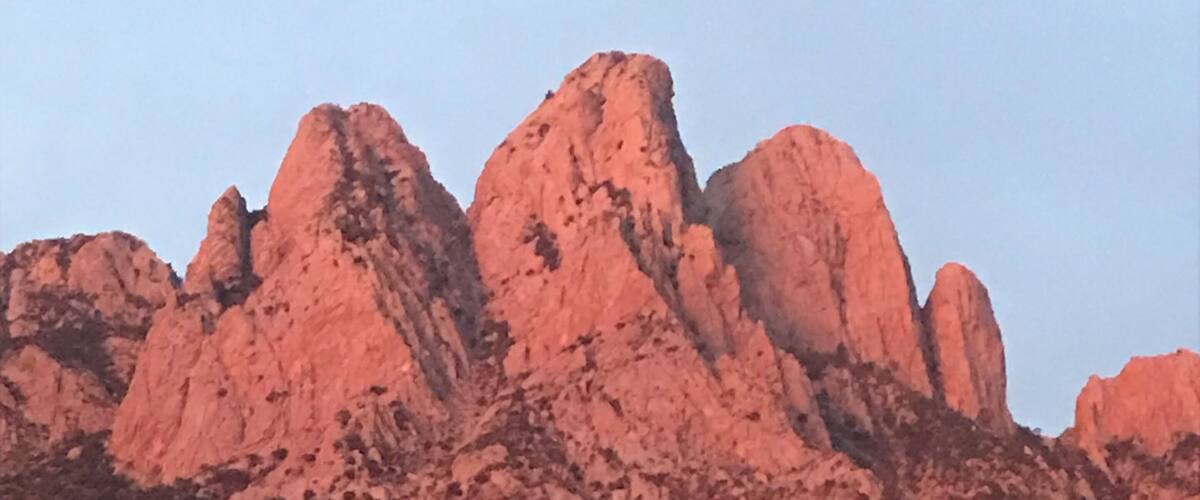 A mountain range with reddish rock formations and sparse vegetation.