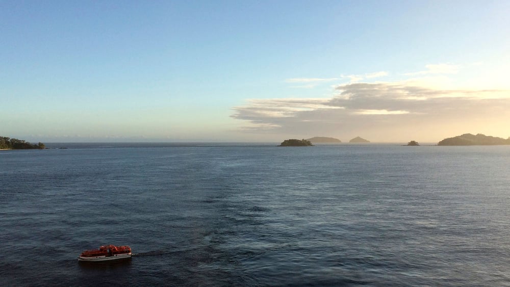 A calm sea with a boat in the foreground and distant islands under a clear sky.