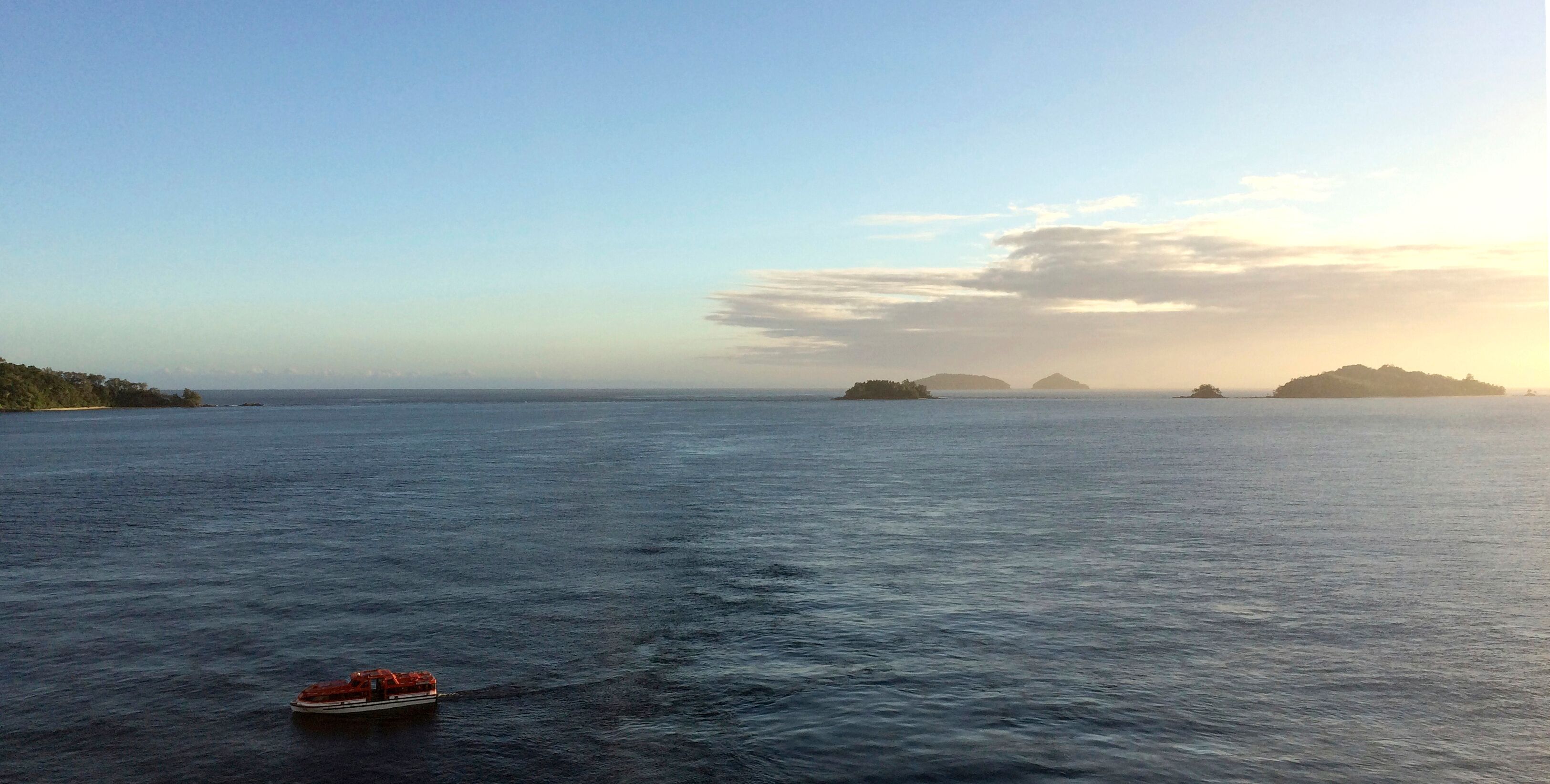 A calm sea with a boat in the foreground and distant islands under a clear sky.