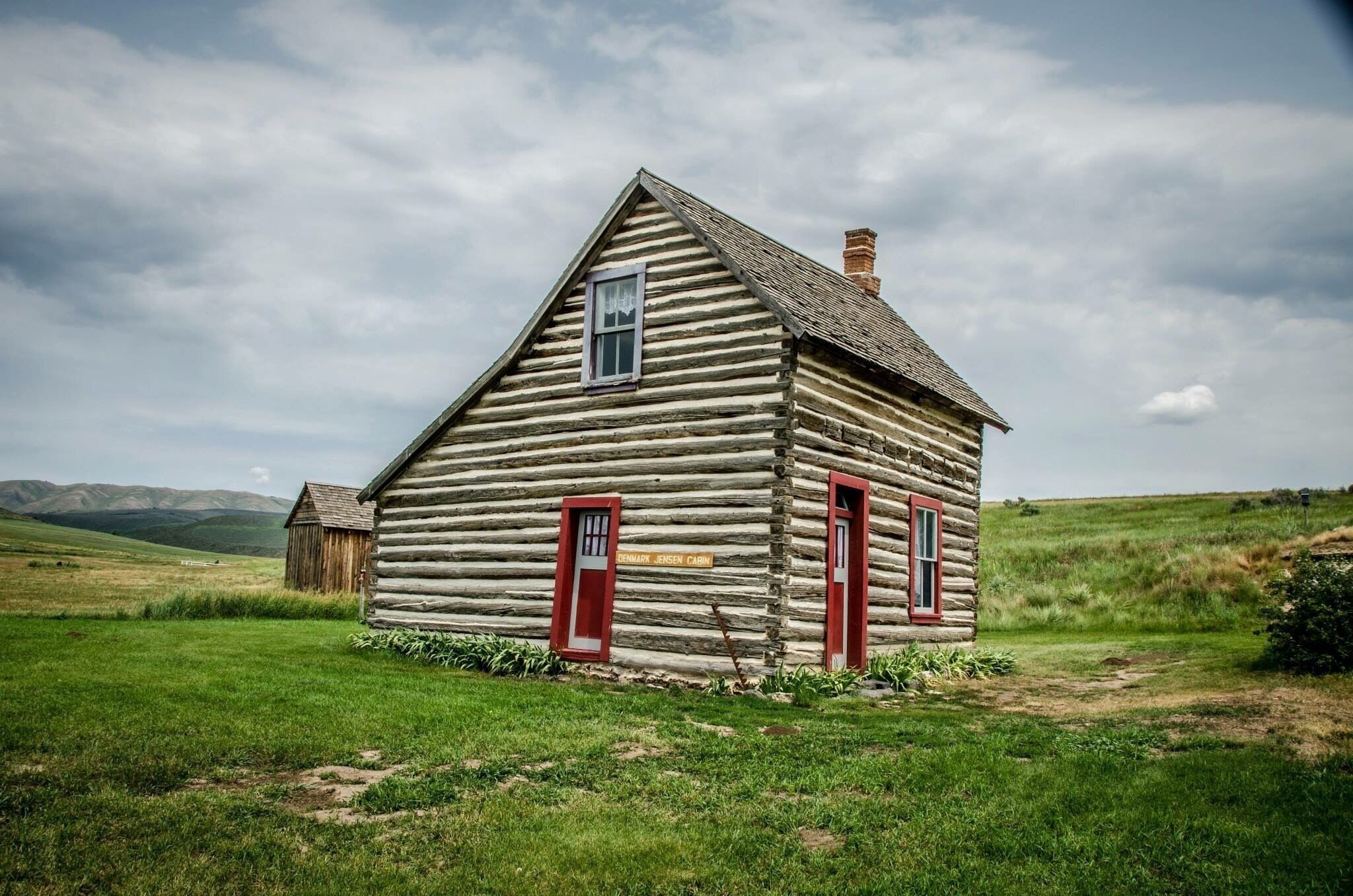 A log cabin with red doors and windows, surrounded by green grass and hills.