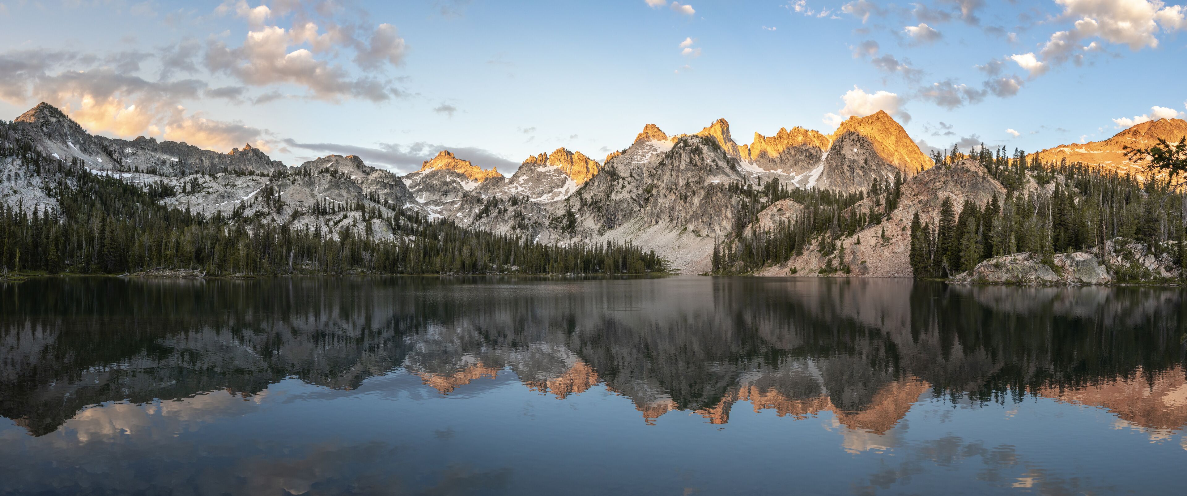 A mountain range reflected in a calm lake with snow-capped peaks and dense forests.