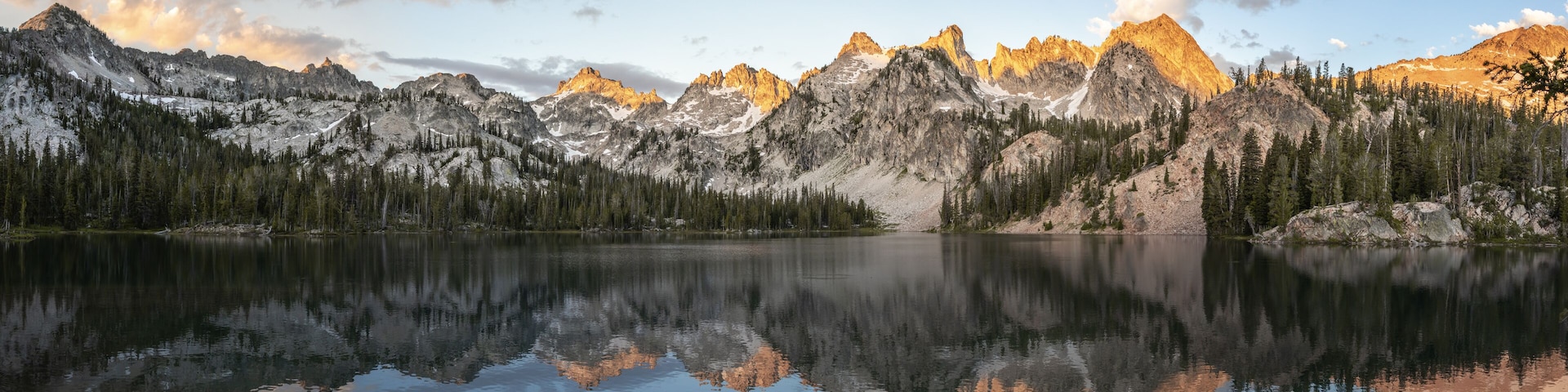 A mountain range reflected in a calm lake with snow-capped peaks and dense forests.