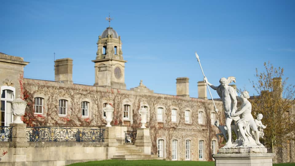 A historic building with a clock tower, a statue of a figure holding a spear, and a fountain in the foreground.