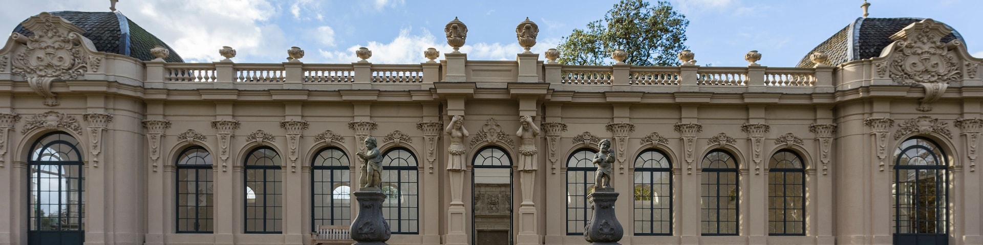 Un edificio imponente con arquitectura ornamentada, que presenta una fachada simétrica, amplias ventanas arqueadas y estatuas.