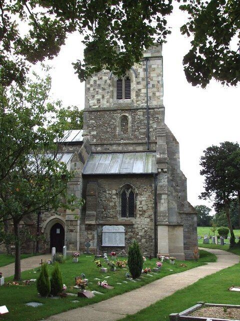 A stone church with a bell tower, surrounded by a cemetery with headstones and flowers.