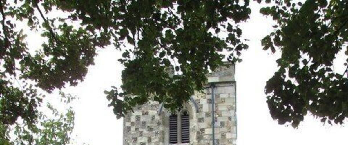 A stone church with a bell tower, surrounded by a cemetery with headstones and flowers.