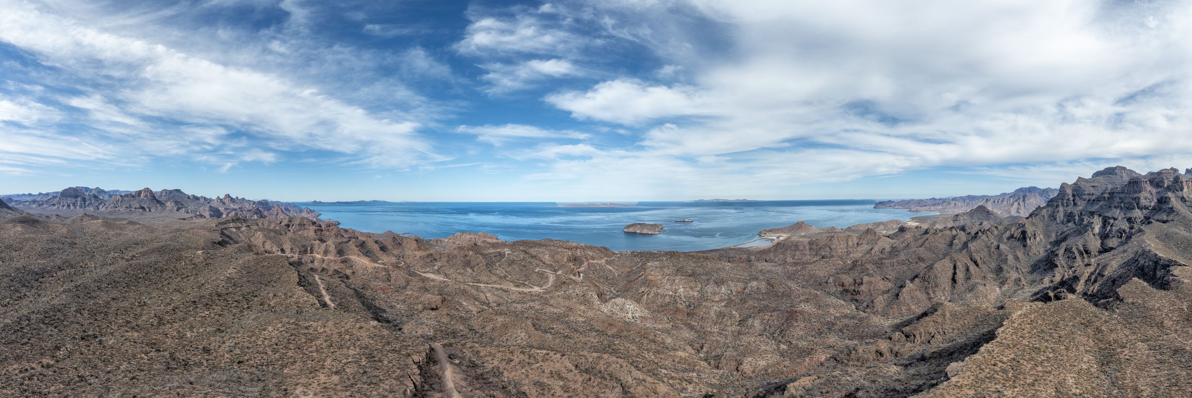 A rugged mountainous landscape with a clear view of a large body of water and distant islands.