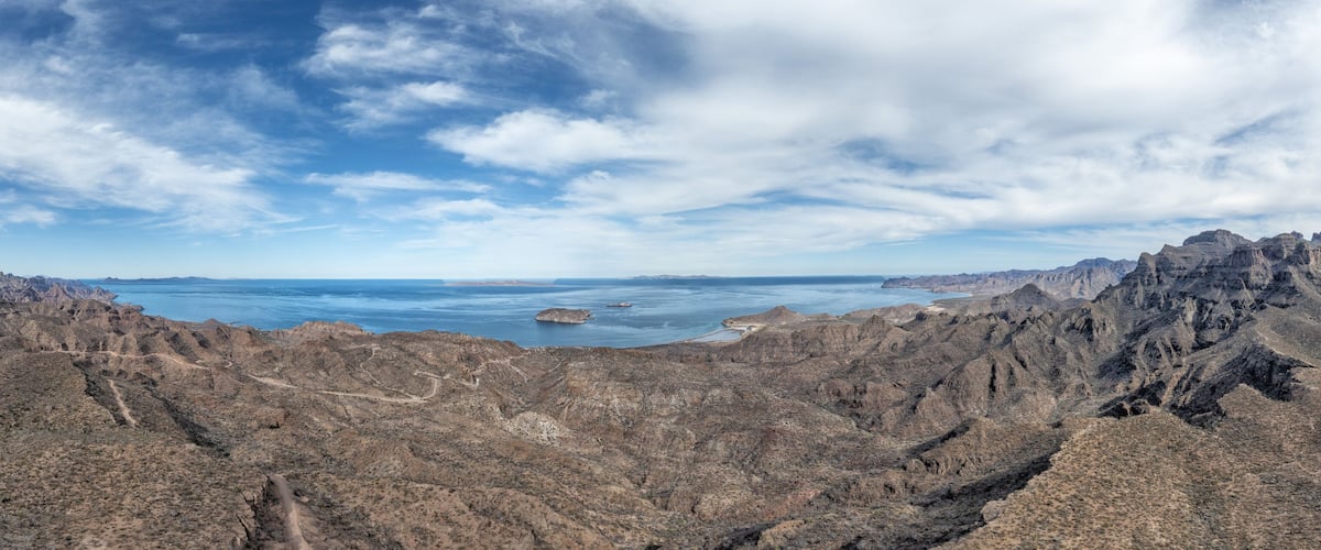 A rugged mountainous landscape with a clear view of a large body of water and distant islands.