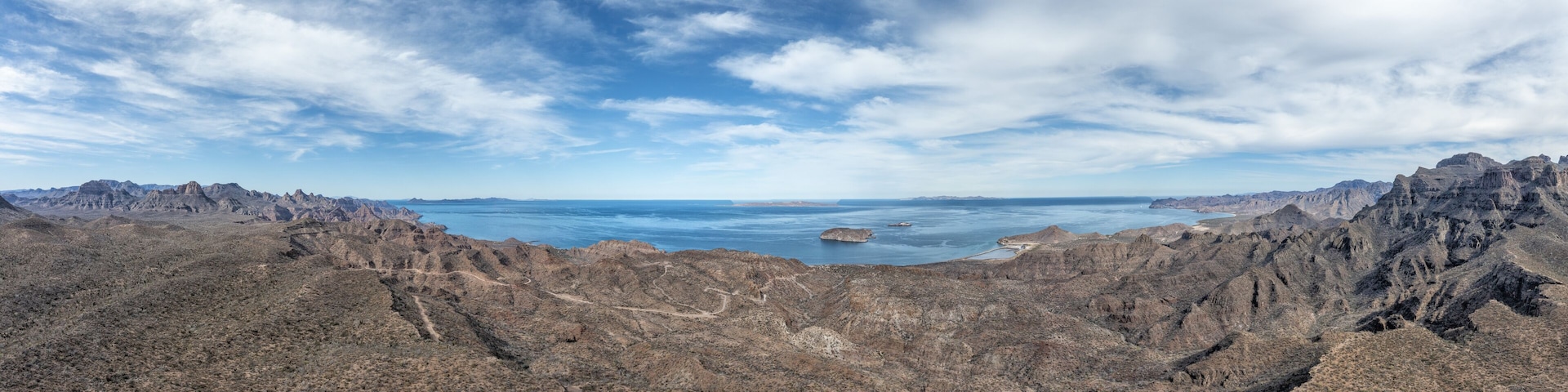 A rugged mountainous landscape with a clear view of a large body of water and distant islands.