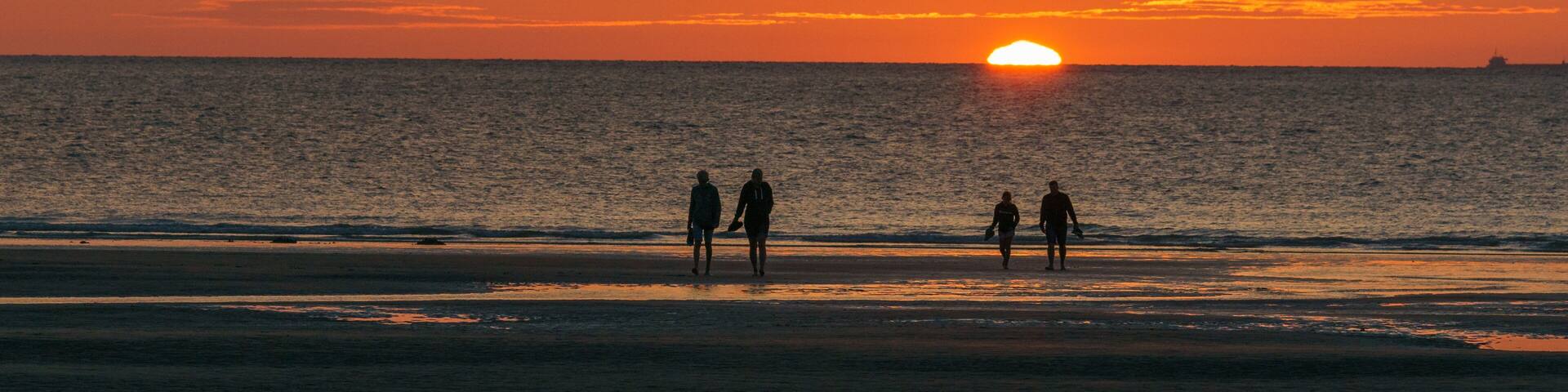 A sunset over the ocean with silhouettes of people walking on the beach.
