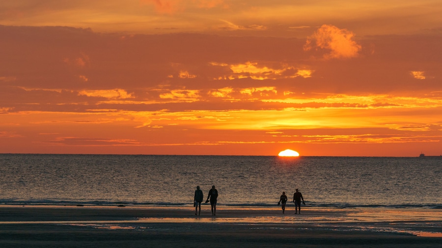 Un atardecer sobre el océano con siluetas de personas caminando por la playa.