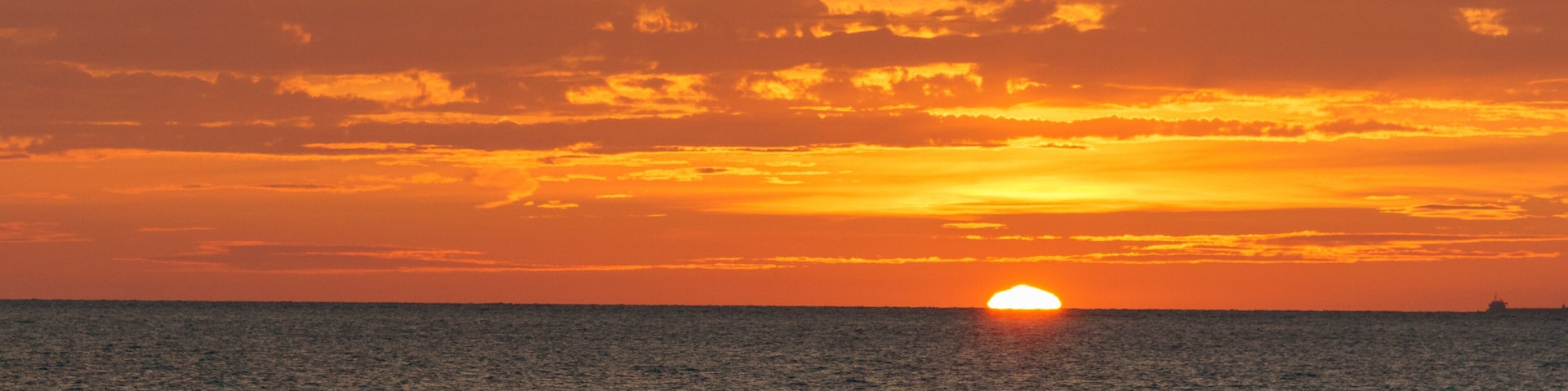 Un atardecer sobre el océano con siluetas de personas caminando por la playa.