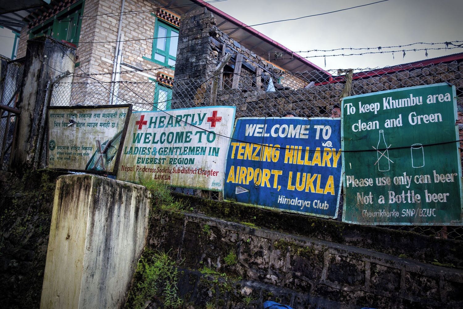 Arriving in Lukla, Nepal. These are the airport signs. At Lukla, there is one tiny runway on the edge of a mountain, a tarmac just big enough to hold 4 small airplanes, and a small airport terminal. You collect your bags right on the tarmac, cross through an opening in this fence, and then begin your journey to Everest Base Camp. It's an adventure just getting here and flying to Lukla was one of the scariest things we have done. Read more about what it is like:  

http://www.earthtrekkers.com/flying-to-lukla-nepal/