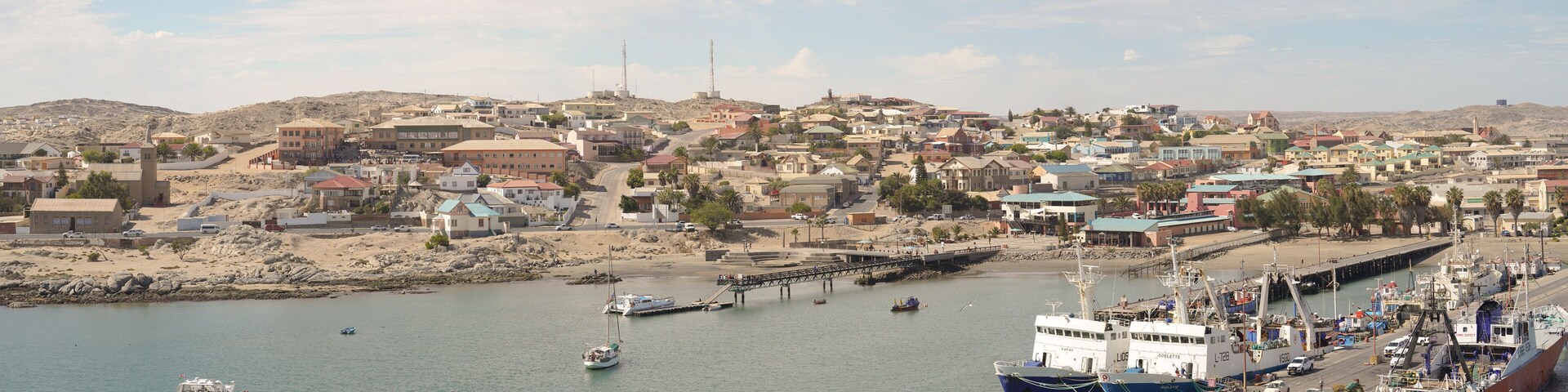 A coastal town with a harbor, boats, and a bridge connecting the town to the mainland.