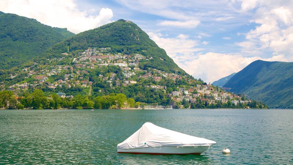 A lake with a boat covered in white, a mountain with a town, and a partly cloudy sky.