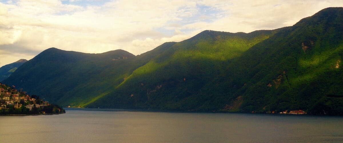 A mountainous landscape with a lake and a small settlement on the left.