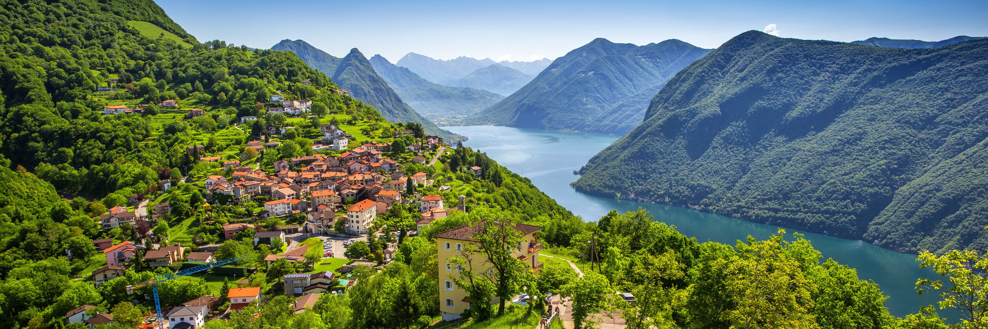 A mountainous village with a lake surrounded by lush greenery and red-roofed houses.