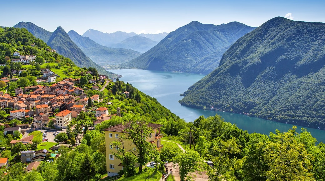 A mountainous village with a lake surrounded by lush greenery and red-roofed houses.