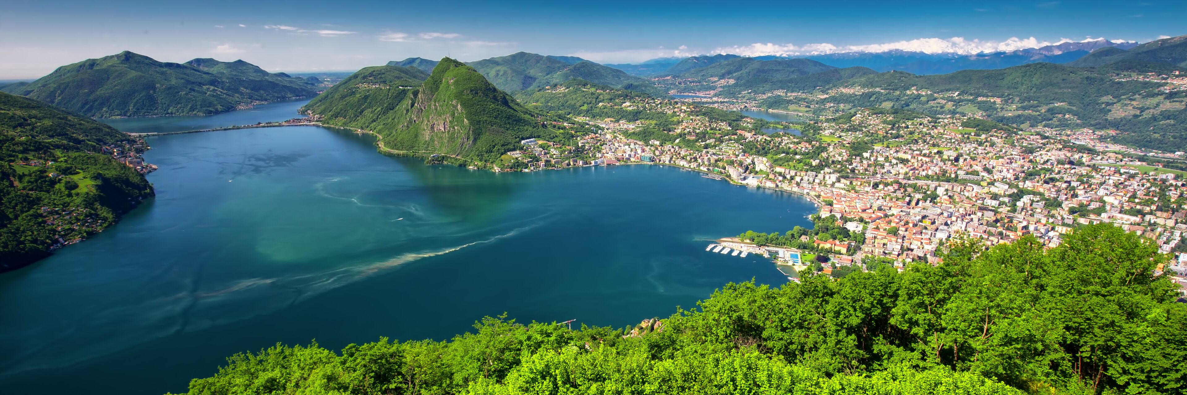 A coastal town with a bay, surrounded by mountains and lush greenery.
