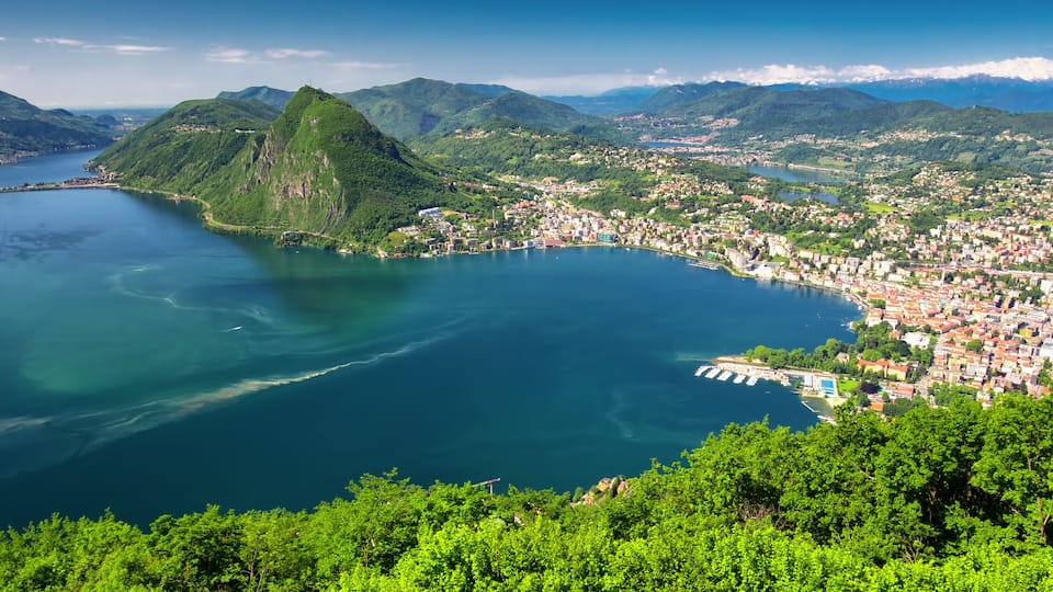 A coastal town with a bay, surrounded by mountains and lush greenery.