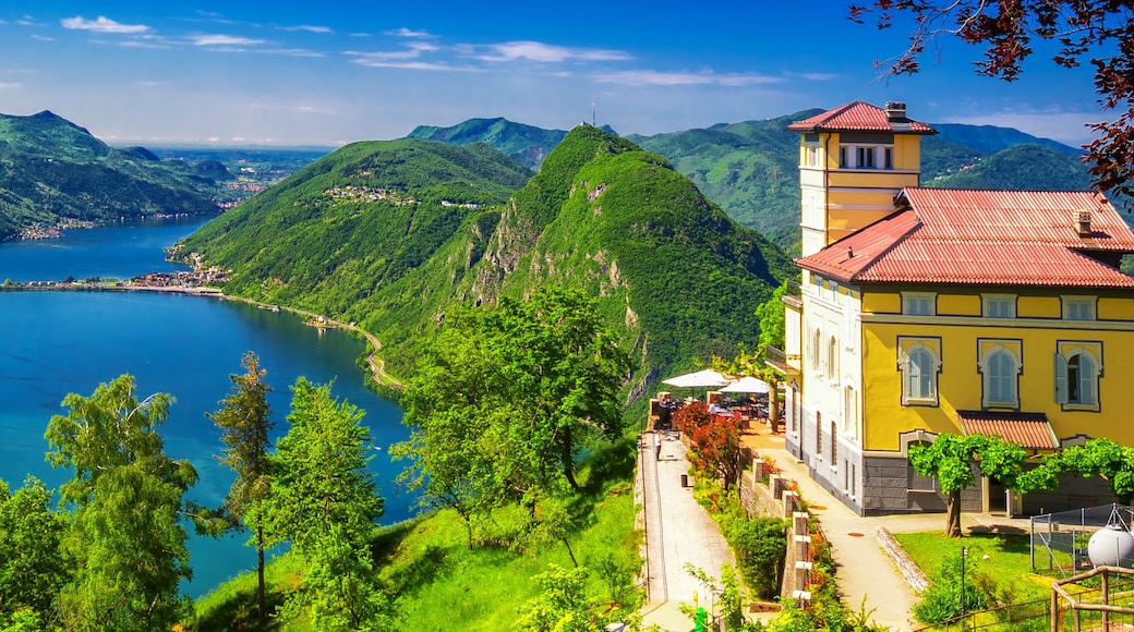 A lake surrounded by lush green hills and a yellow building with a red roof.