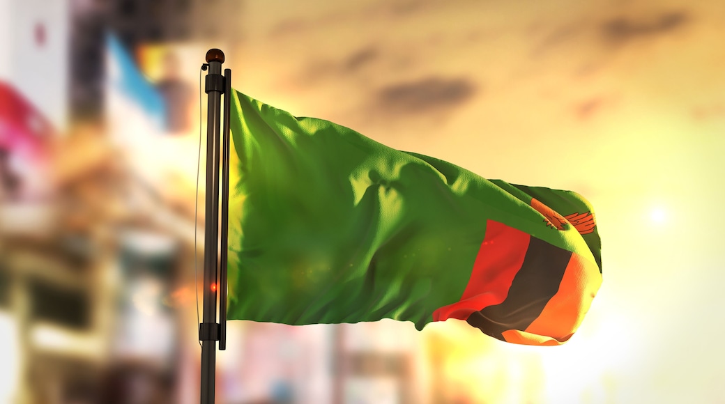 Zambia Flag Against City Blurred Background At Sunrise Backlight