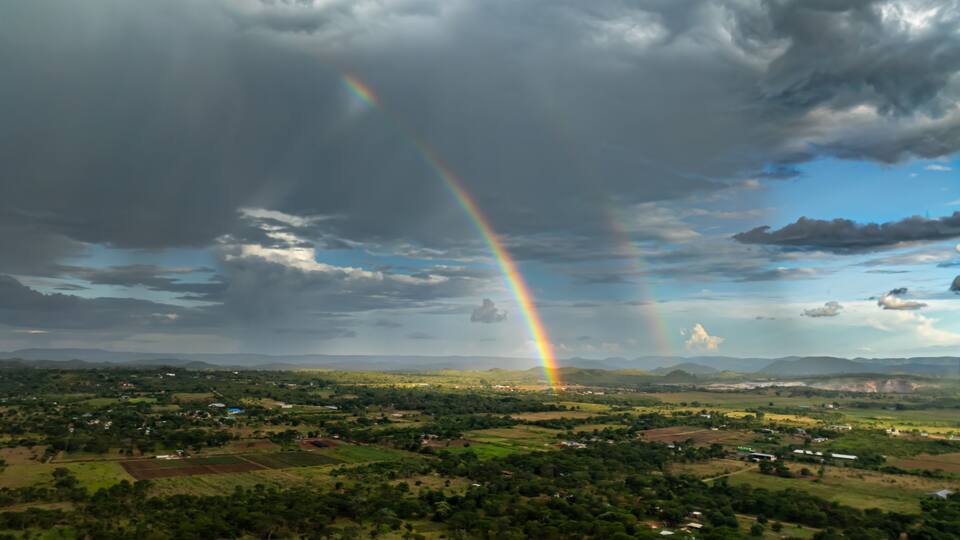 A landscape with a rainbow, green fields, and scattered houses.