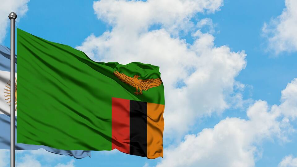 Two flags waving against a blue sky with clouds.