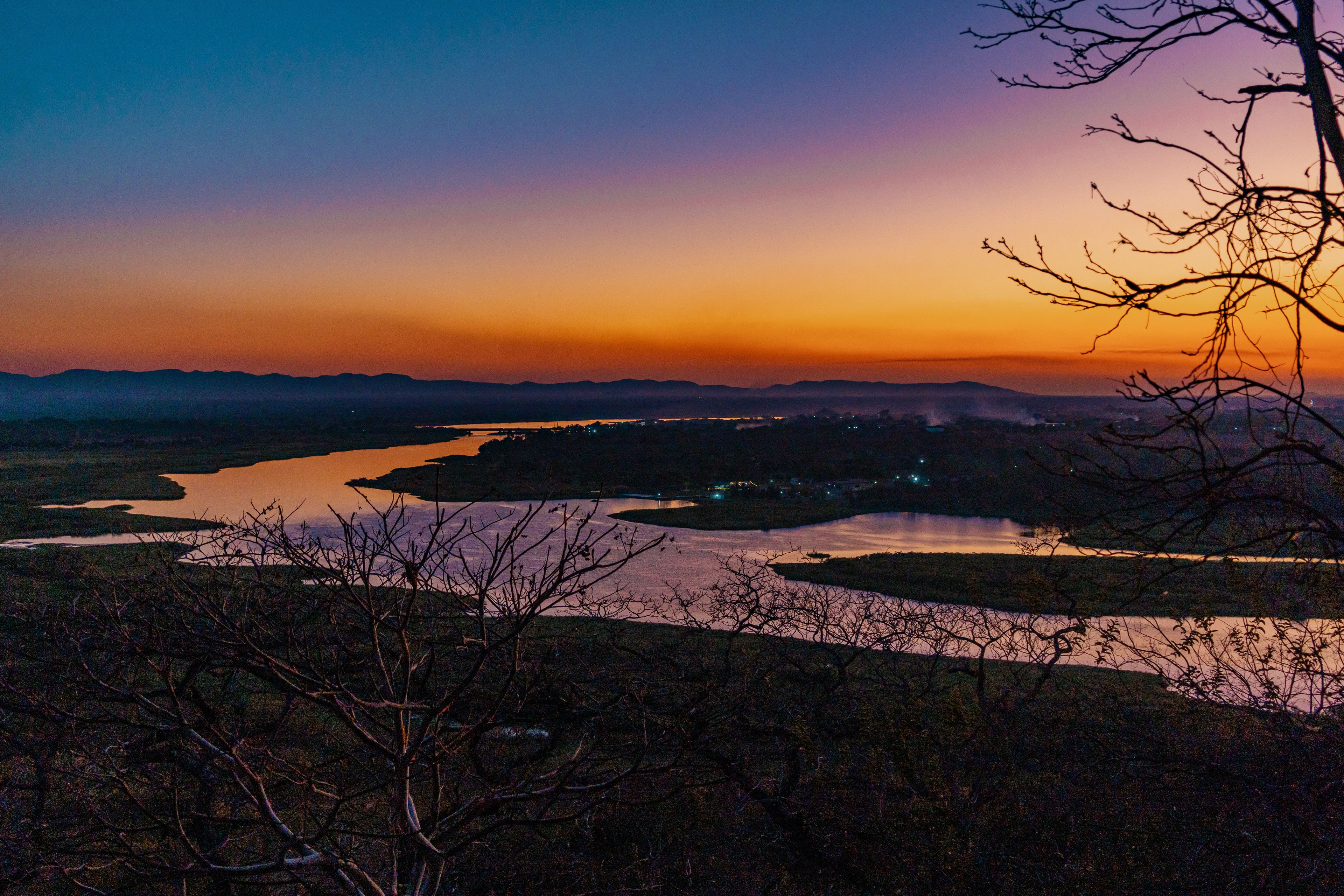 Kafue, Lusaka Province, Zambia - 19 July 2026: Aerial view of the Kafue River winding through the landscape at sunset with silhouettes of trees in the foreground and a vibrant orange sky.