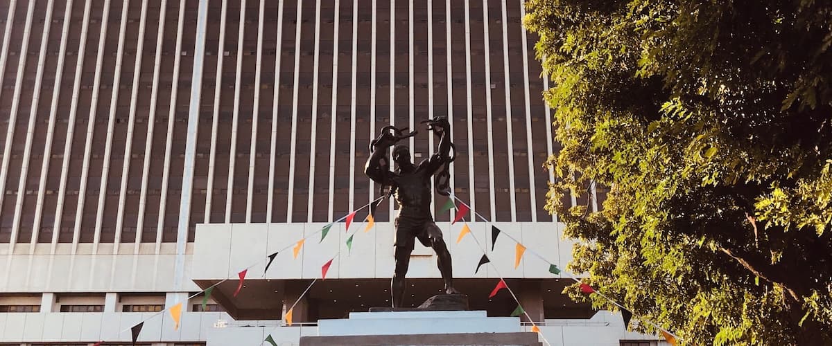 A statue of a man with raised arms in front of a building with vertical lines and the word "FREEDOM" on the gate.