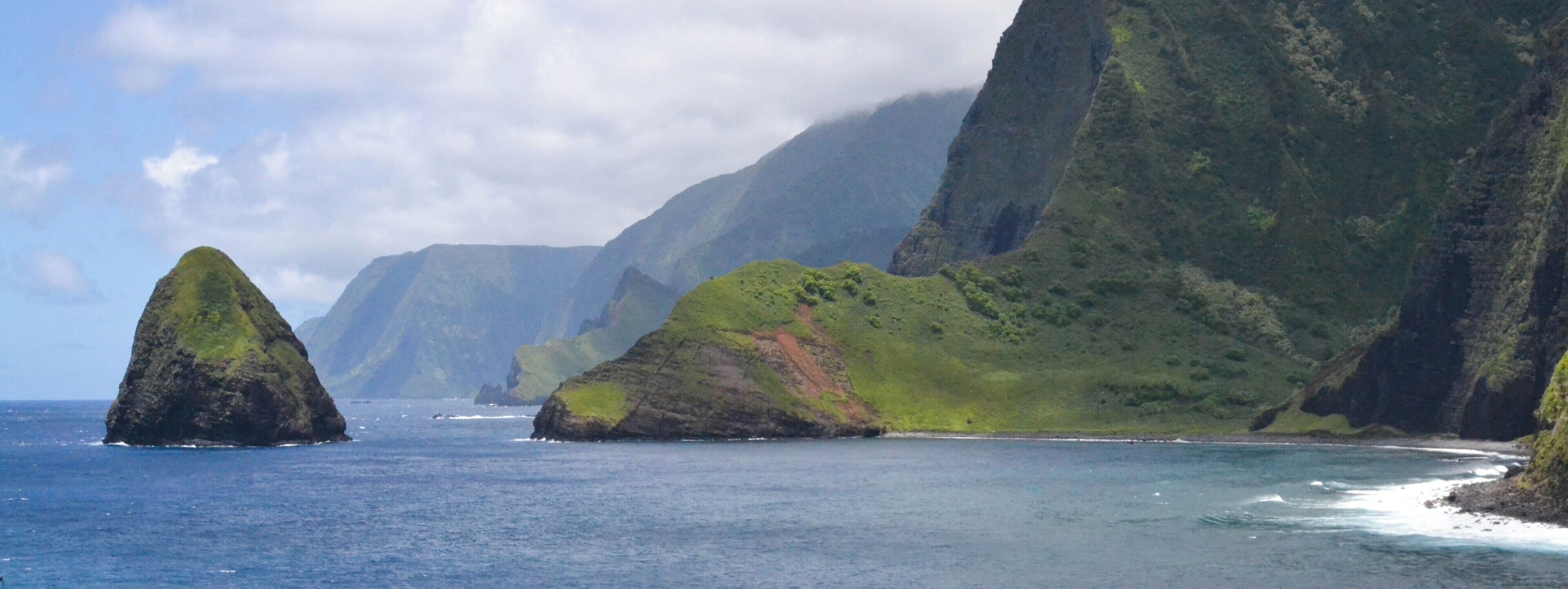 A coastal landscape with a prominent green hill and a smaller rock formation in the sea.
