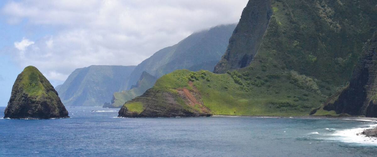 A coastal landscape with a prominent green hill and a smaller rock formation in the sea.