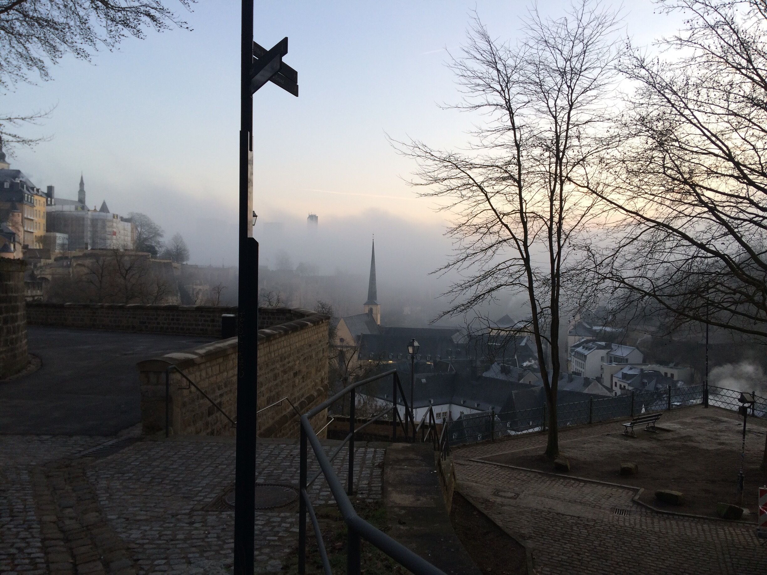 A foggy cityscape with a prominent church spire, cobblestone streets, and a guard tower.