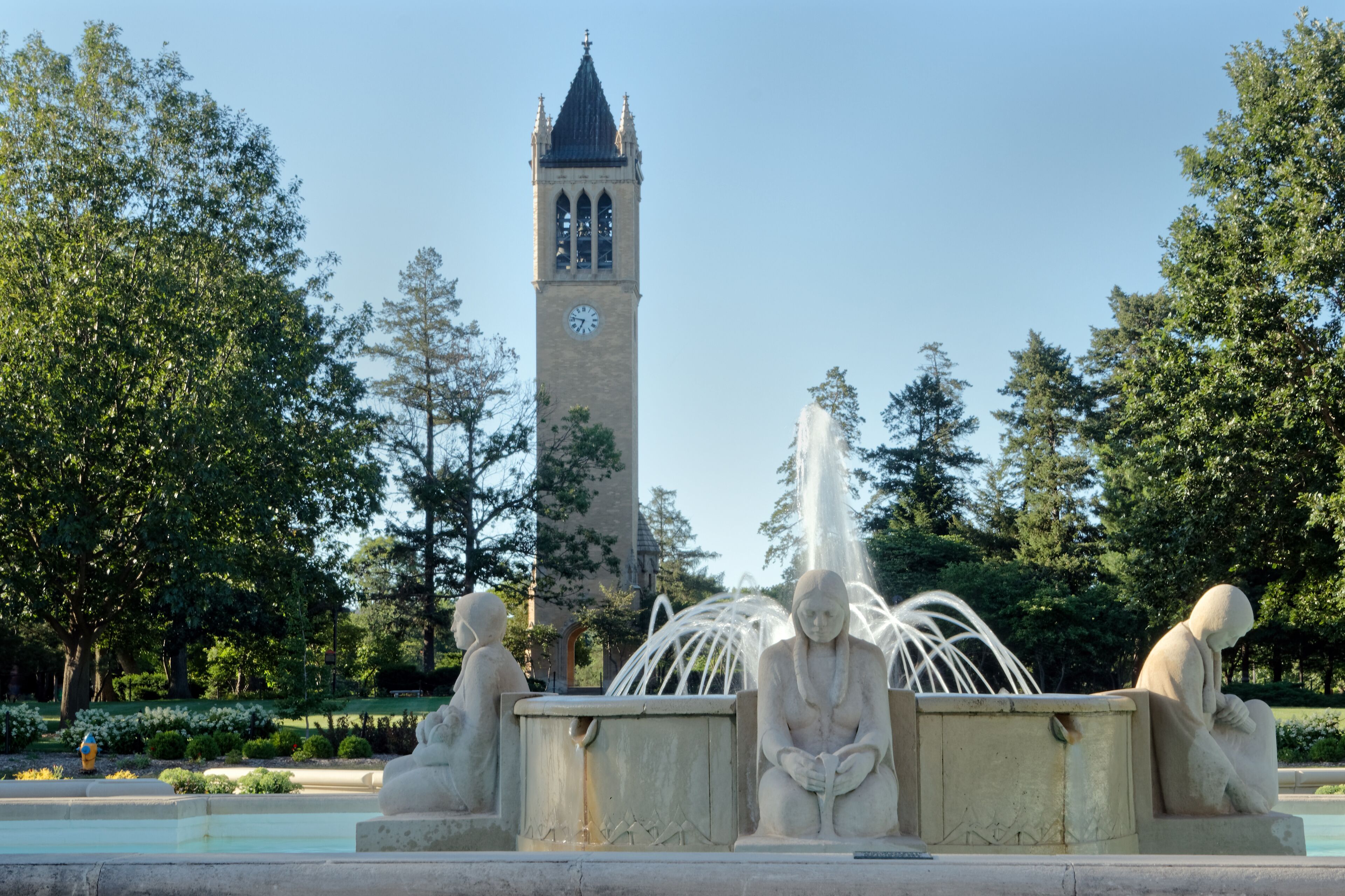 A park with a clock tower, a fountain, and statues.