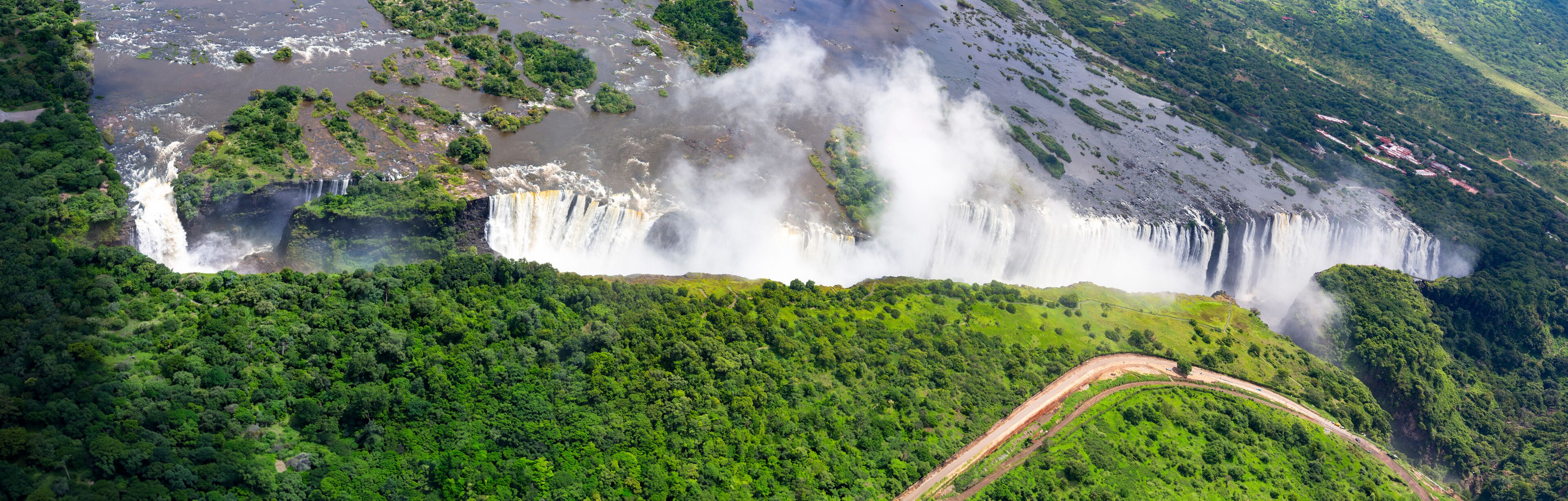 A large waterfall cascading down a lush green hillside, surrounded by dense forest.