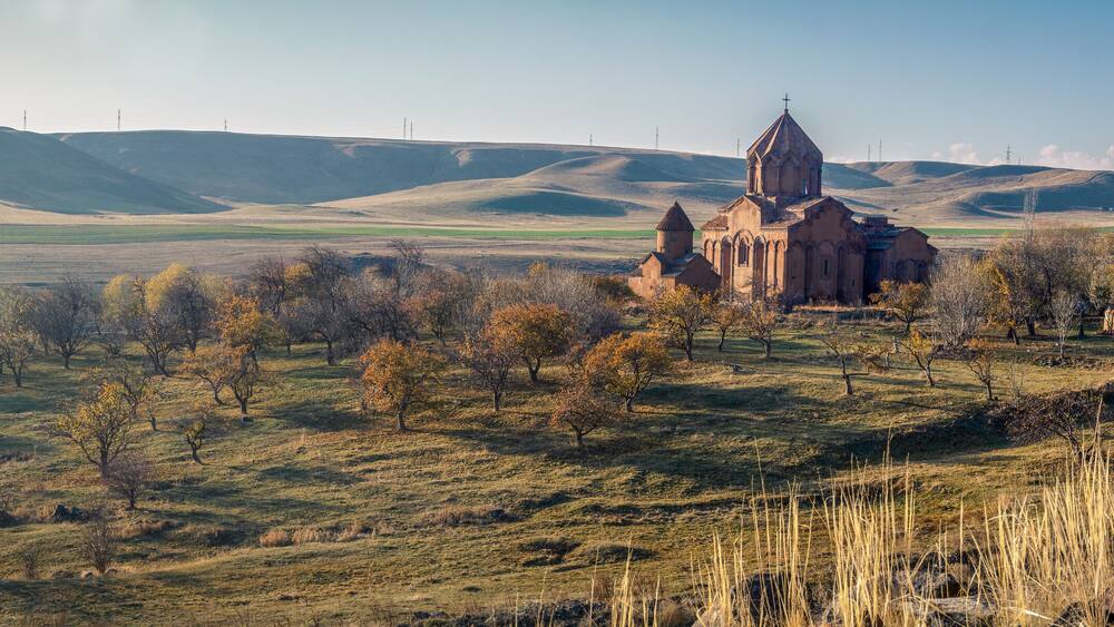 Eine Kirche, umgeben von sanften Hügeln und vereinzelten Bäumen.