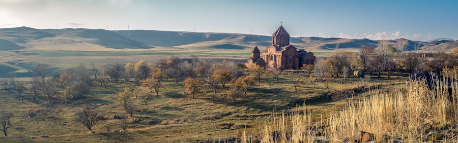 Una iglesia rodeada de colinas ondulantes y escasos árboles.