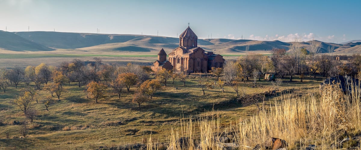 A church surrounded by rolling hills and sparse trees.