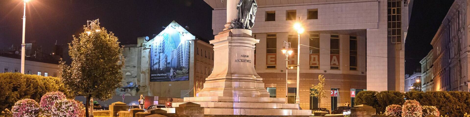 A statue in a square with steps leading up to it, surrounded by trees and bushes.