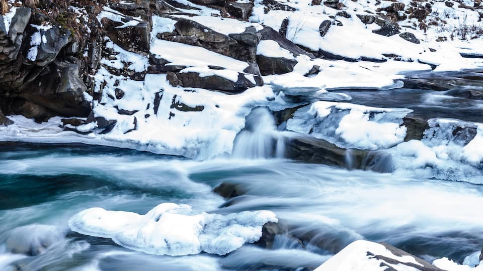 A fast-flowing river with ice formations and rocky terrain.