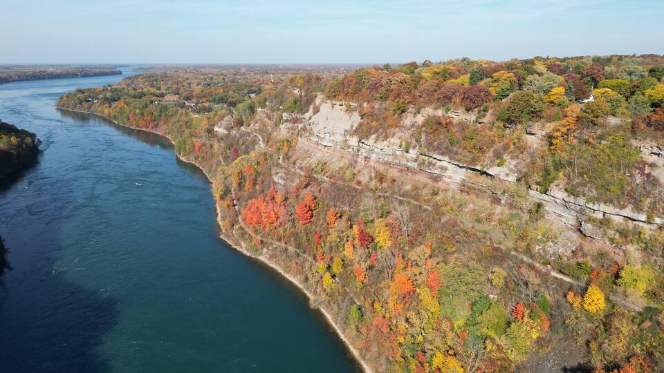 Aerial over the Niagara River and gorge between Lewiston, New York, United States and Ontario, Canada towards Lake Ontario. Shot during an autumn afternoon with colorful fall foliage trees in October.