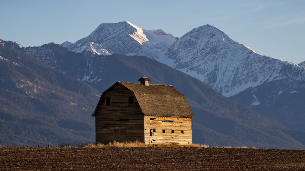 Ein hölzernes Getreidespeicher in einem Feld, im Hintergrund verschneite Berge.