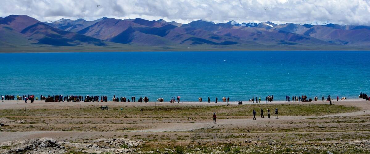 A vast lake with mountains in the background and a group of people on the shore.