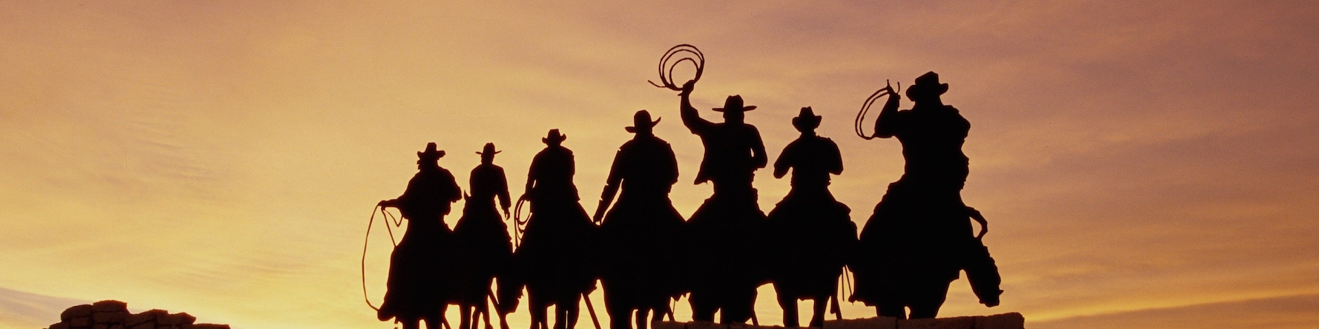 Silueta de vaqueros a caballo contra un cielo al atardecer.