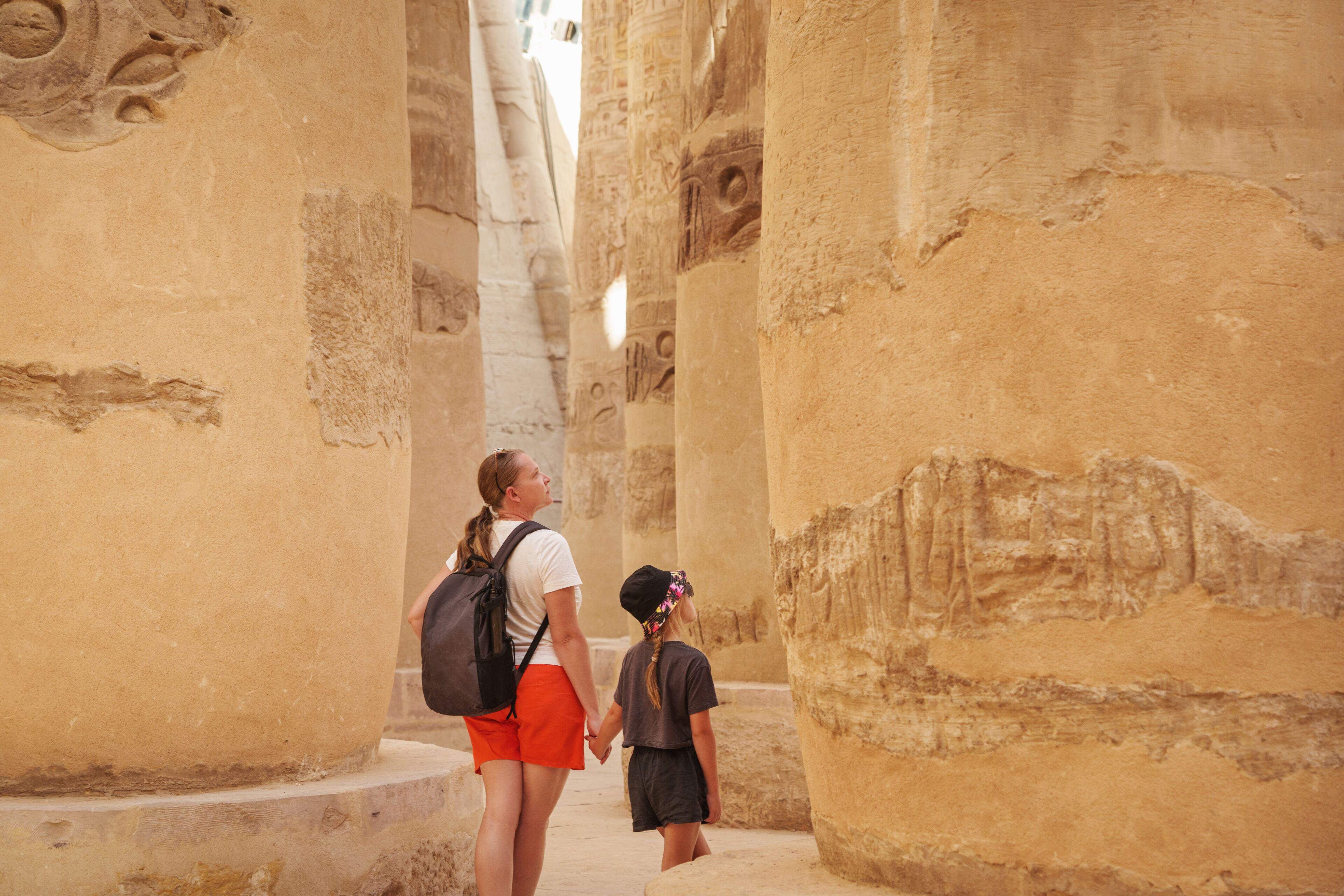 Two people walking through ancient stone columns with hieroglyphs.