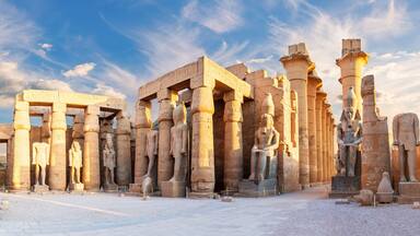 Gamle egyptiske ruiner med høje stensøjler og statuer under en klar himmel.