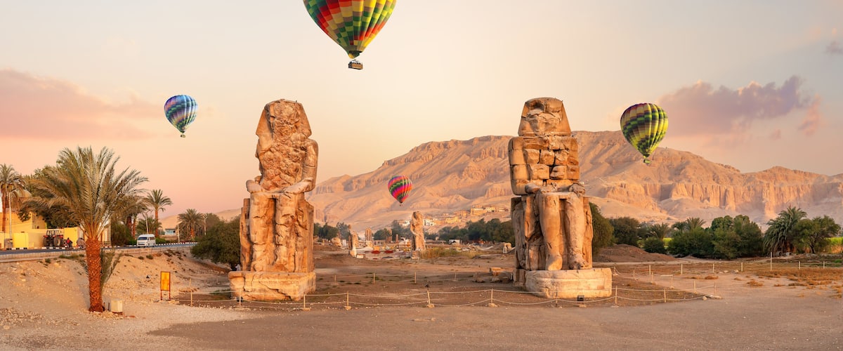 A desert landscape with ancient stone statues and hot air balloons in the sky.