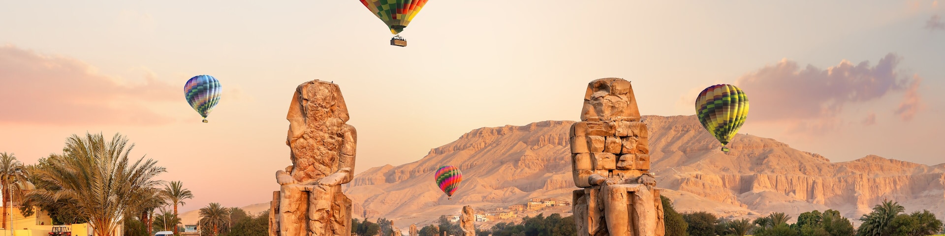A desert landscape with ancient stone statues and hot air balloons in the sky.